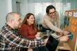 Tři kolegové v coworkingu plánují úkoly u nástěnky s barevnými lepicími papírky, usměvaví a uvolnění.